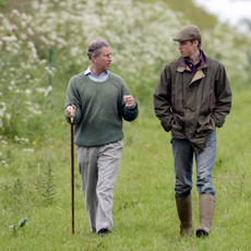 Prince William, In Countryman Outfit Of Tweed Cap And Waxed Jacket And With His Hands In His Pockets, Visits Duchy Home Farm With Prince Charles Who Is Holding A Shepherd's Crook Walking Stick