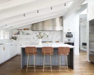 White kitchen with gray island with three bar chairs and wood floor