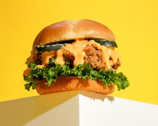 Fried chicken sandwich on bun with lettuce, pickle and sauce. Yellow background.