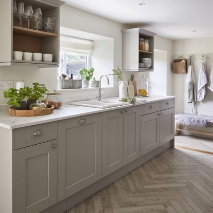 Light grey shaker kitchen with gold hardware and chevron flooring.