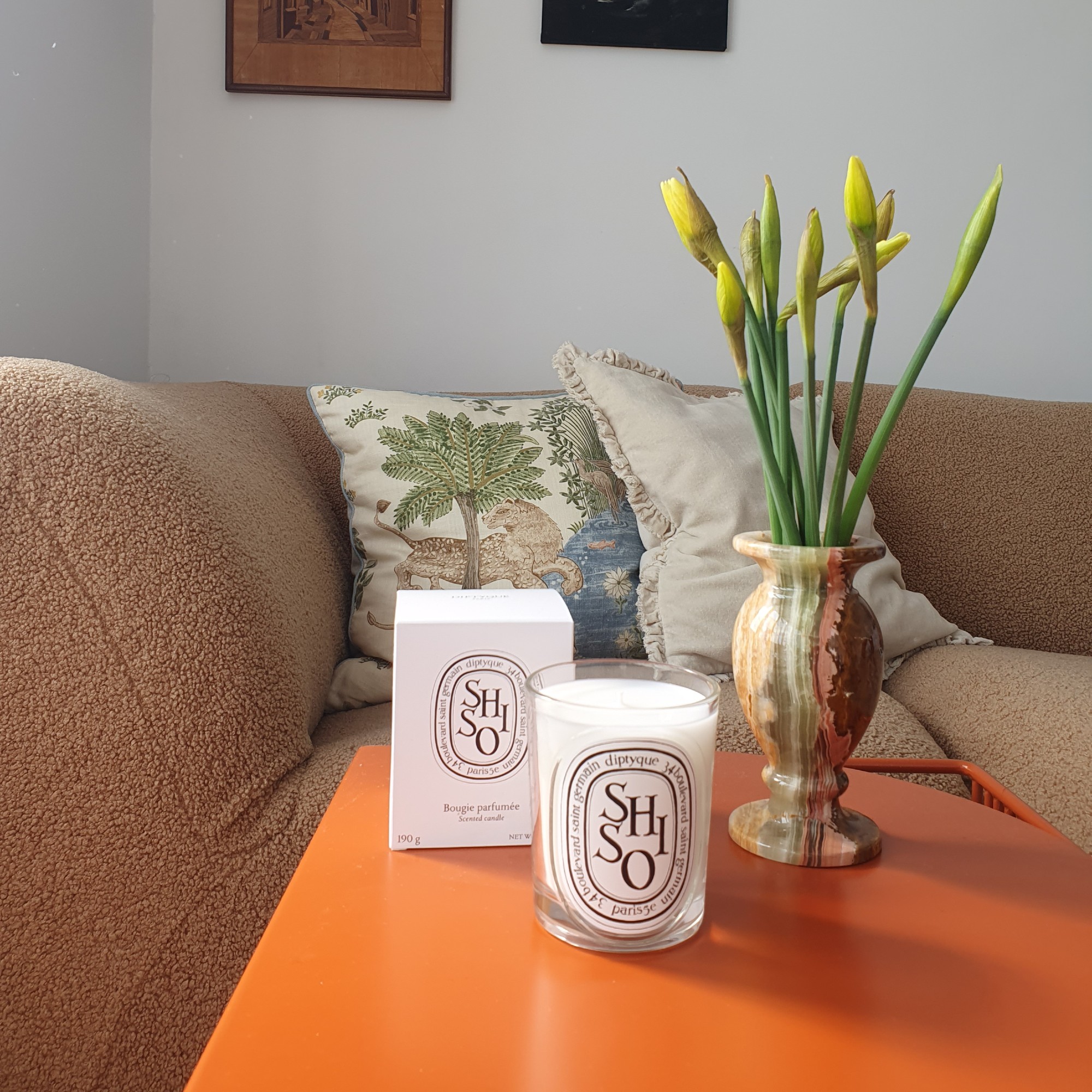 Diptyque's Shiso candle with the box next to it on Sara Hesikova's orange metal coffee table in front of a beige sofa