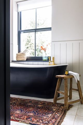 Woven bath mat in front of a black tub