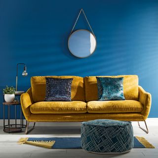 A gold coloured sofa on a white wooden floor in a room with bold blue walls