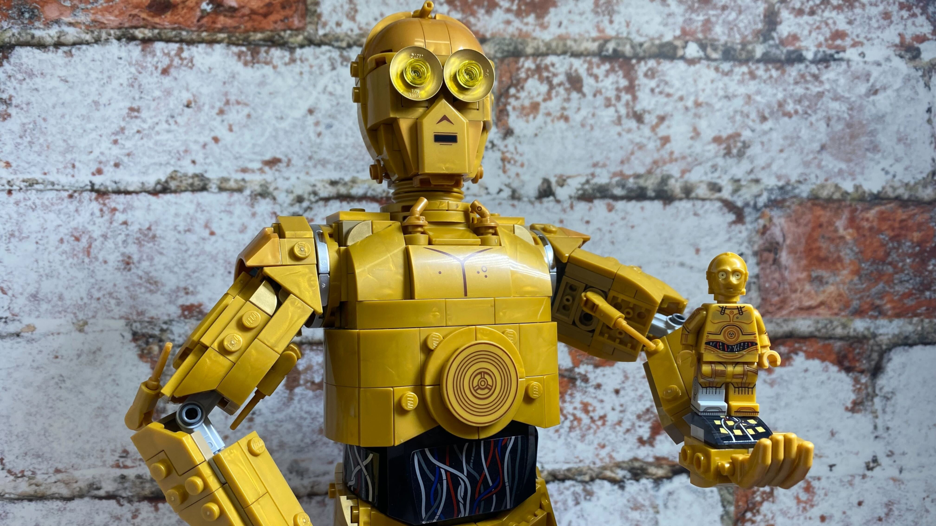 Lego C-3PO sostiene una minifigura de Lego C-3PO más pequeña, todo en una pared de ladrillos