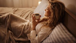 Woman drinking a cup of tea in bed instead of alcohol and smiling to herself