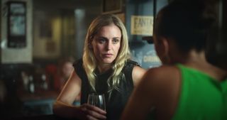 Lena (Denise Gough) is sitting in a bar with a glass of wine in her hand, talking to another woman who has her back to the camera and is out of focus