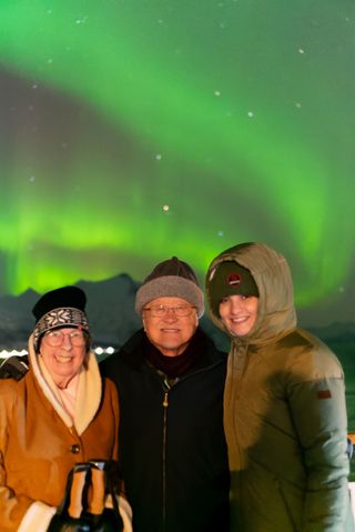 Three people smiling with the northern lights in the sky behind.