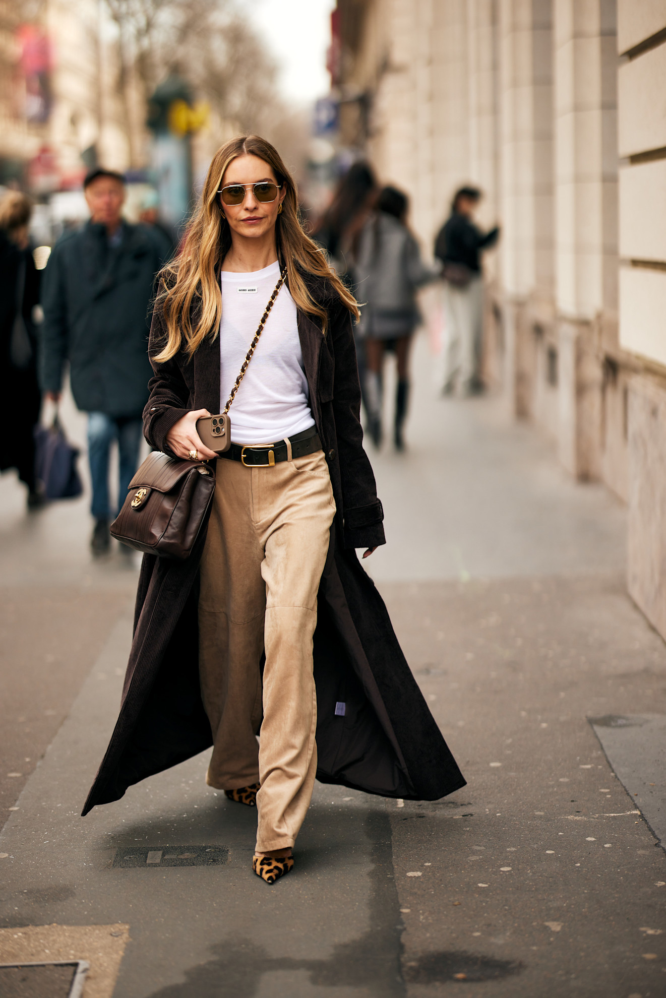 fashion week attendee wears sunglasses, white t-shirt, black coat, camel pants, leopard print shoes