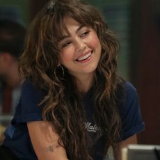 Mika Abdalla as Allie smiling and leaning over a counter at work in 'Off Campus.'