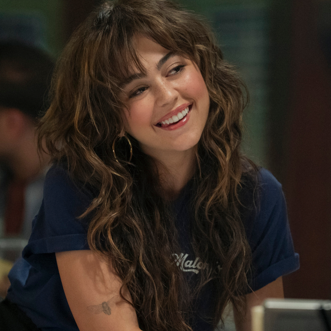 Mika Abdalla as Allie smiling and leaning over a counter at work in 'Off Campus.'