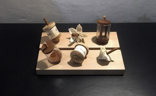 White textured wall, black worktop, small wooden board with six wooden and glass objects on display