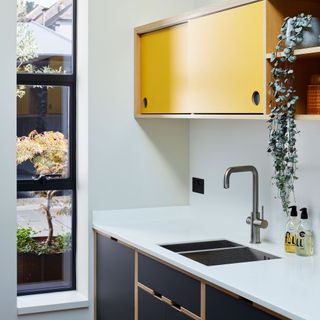 small utility room with long vertical window, yellow cabinetry and a sink