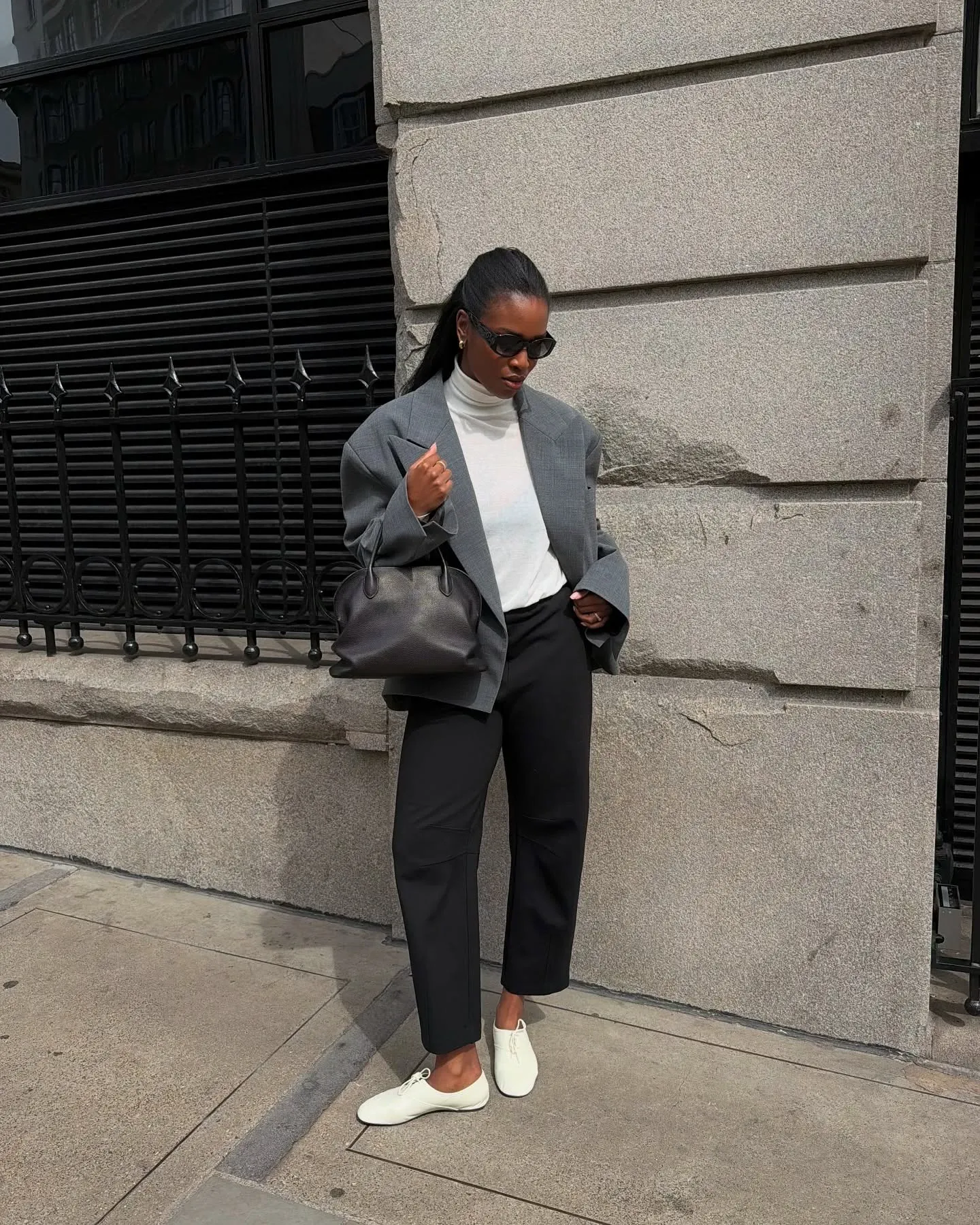 Woman wearing black pants, grey blazer, white turtleneck, and white jazz shoes.