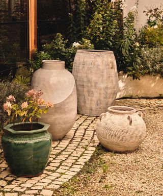 Selction of oversized pots on paved area, one green, the rest stoneware,