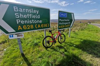 The Wilier Granturismo SLR road bike leaning up between two road signs on grass with hills and blue sky in the background