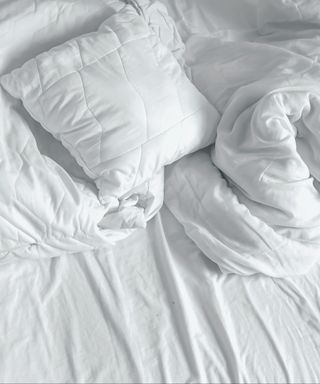 A birds eye view of a white messy duvet with white sheets below it