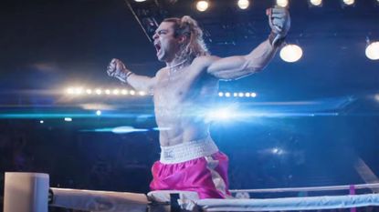 A wrestler stands in the ring with his arms raised in triumph