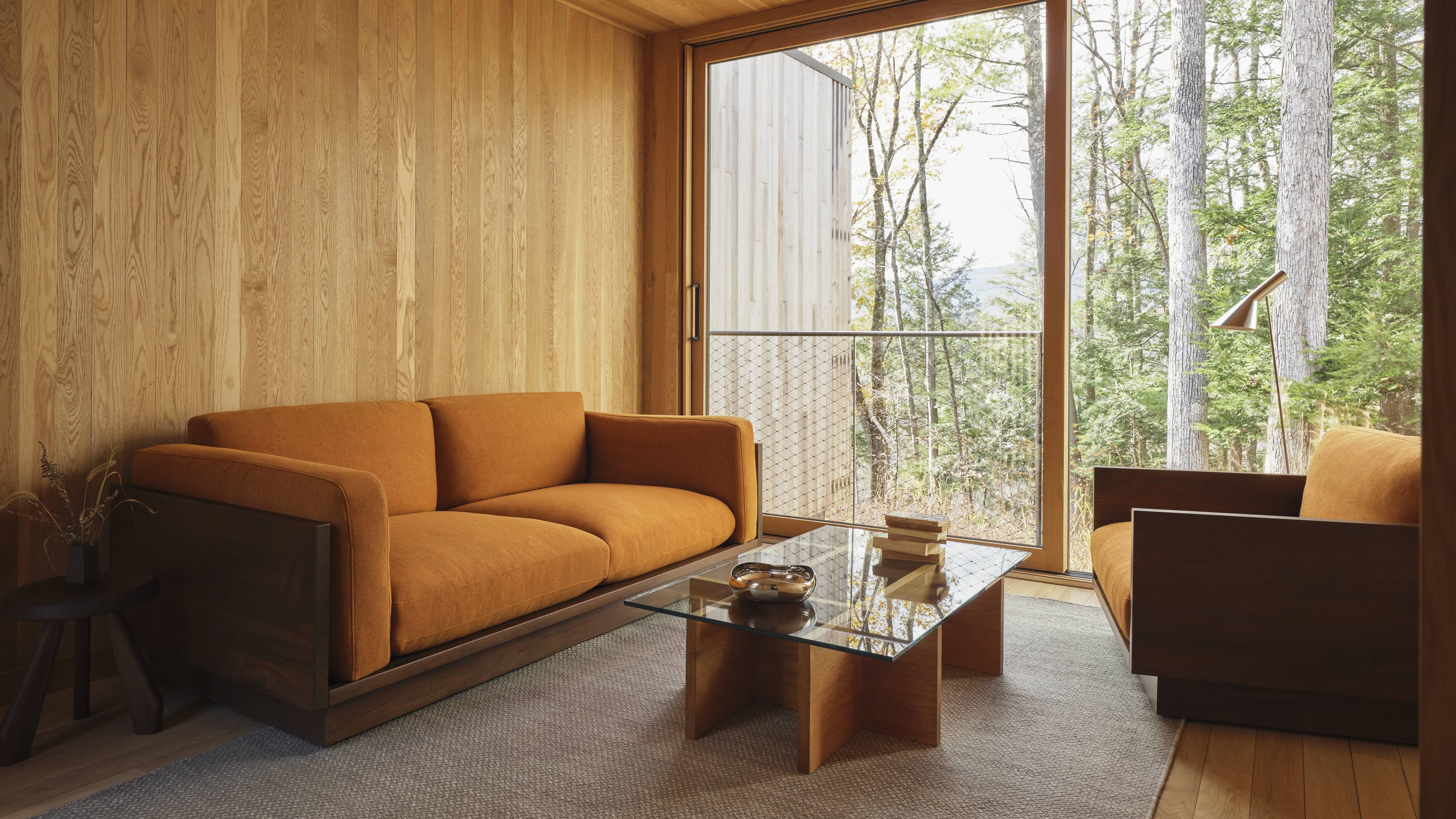 In Piaule hotel&#039;s double cabins, modernist furniture in warm tones sit in front of a window wall overlooking the forest.