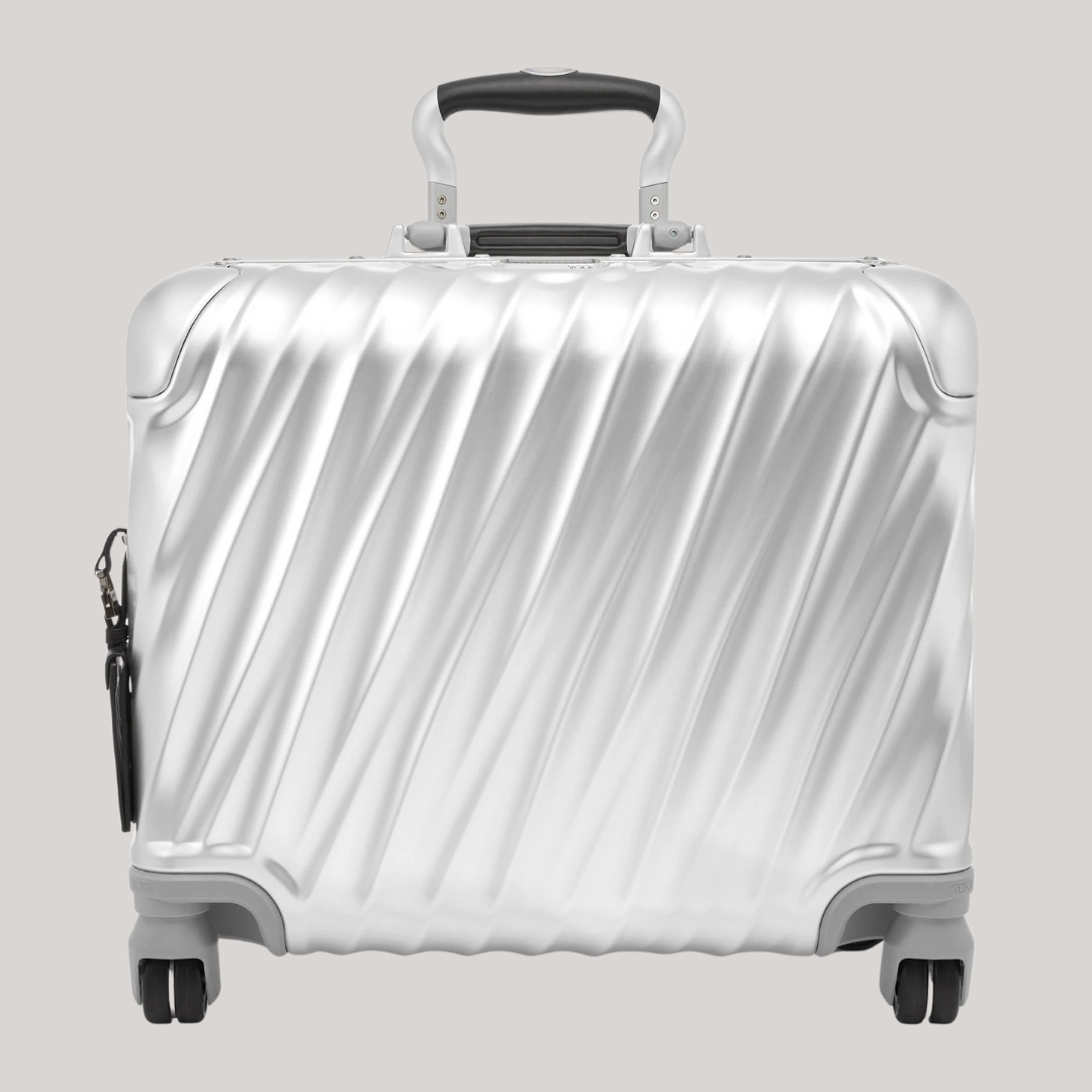 A horizontal carry-on case in aluminum features black and dark grey detailing and a textural, wavy surface while sitting against a pale gray background.