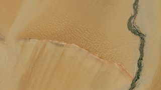An image of Earth from space, with bright brown land streaked with a dark green river on the right side of the image with a curved ridge from left to right meeting the river toward the bottom of the image
