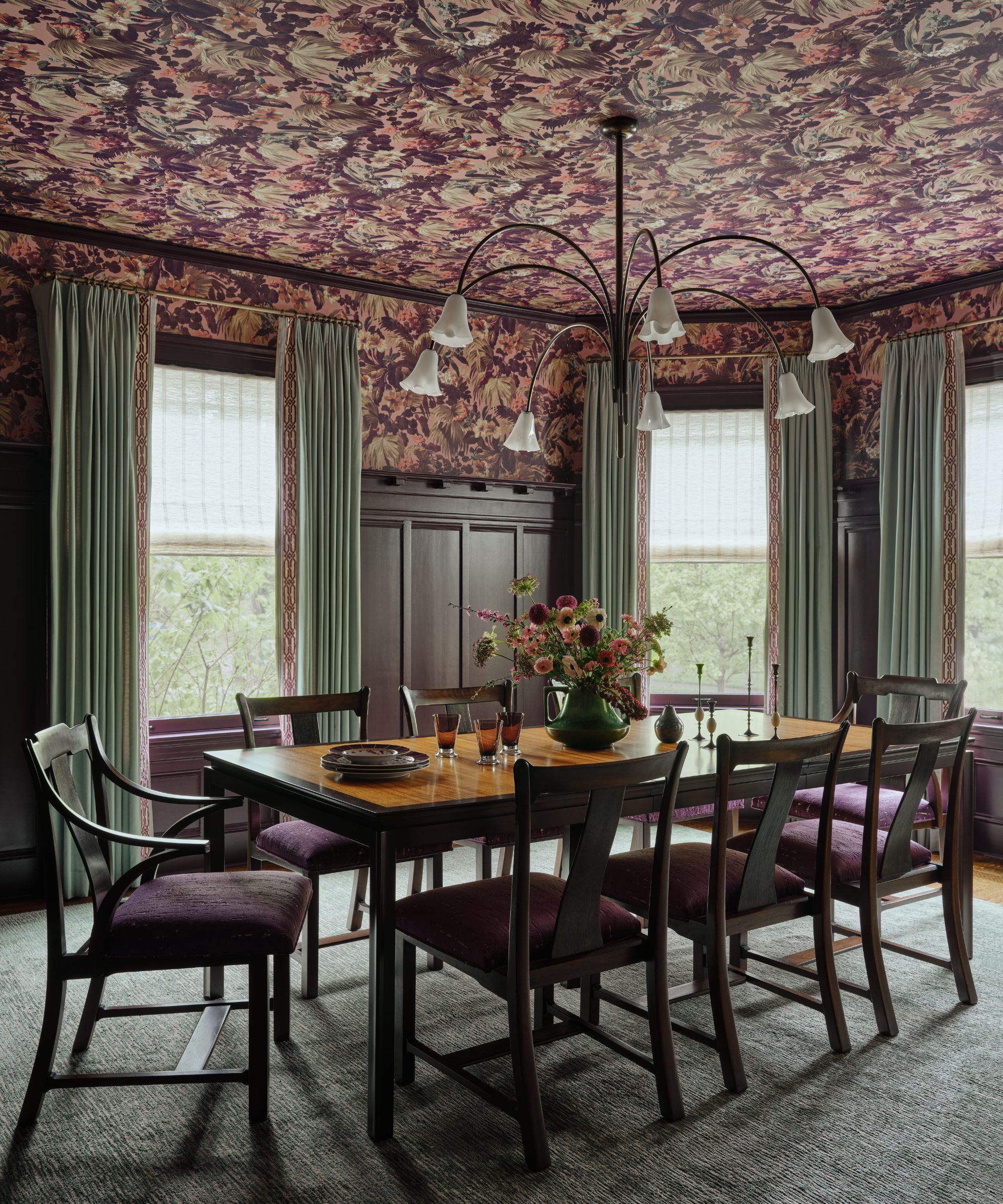 Moody dining room featuring dark wood paneling, purple upholstered chairs, and a matching dark floral wallpapered ceiling.