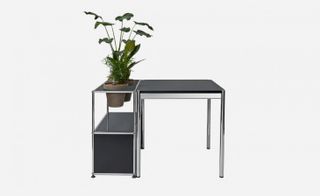Small black and chrome home office desk by USM. On the left side are spaces for plant pots, photographed with two plants with green foliage