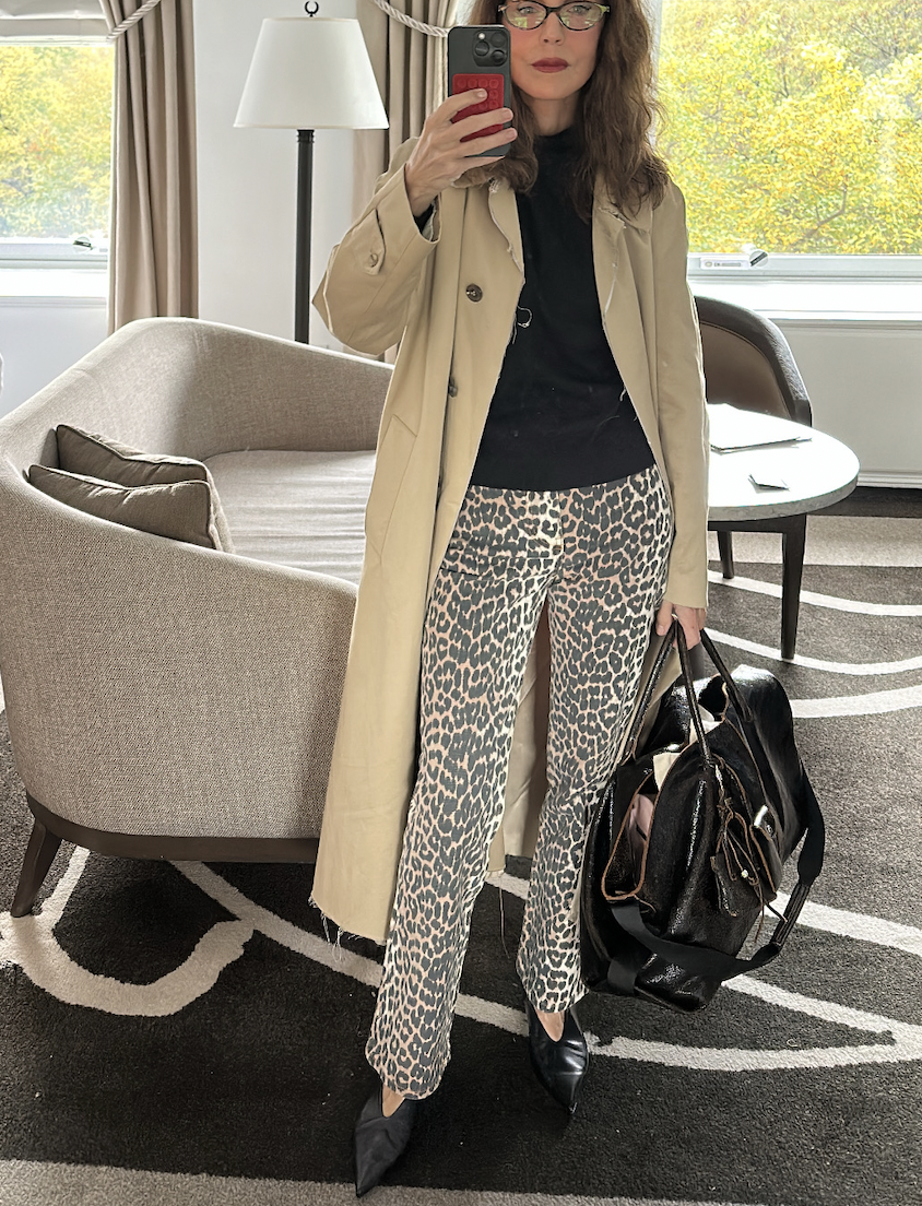 Larissa Mills wearing a black shirt, cheetah pants, a trendh coat, and black leather large tote bag.