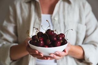 a person holding a bowl of cherries