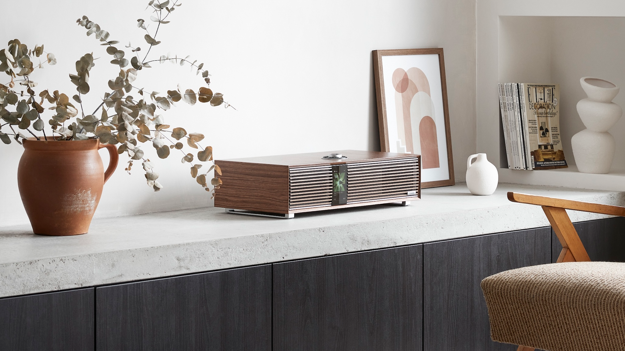 The Ruark R410 in a neutrally decorated room with a flower pot, picture frame and some books around it