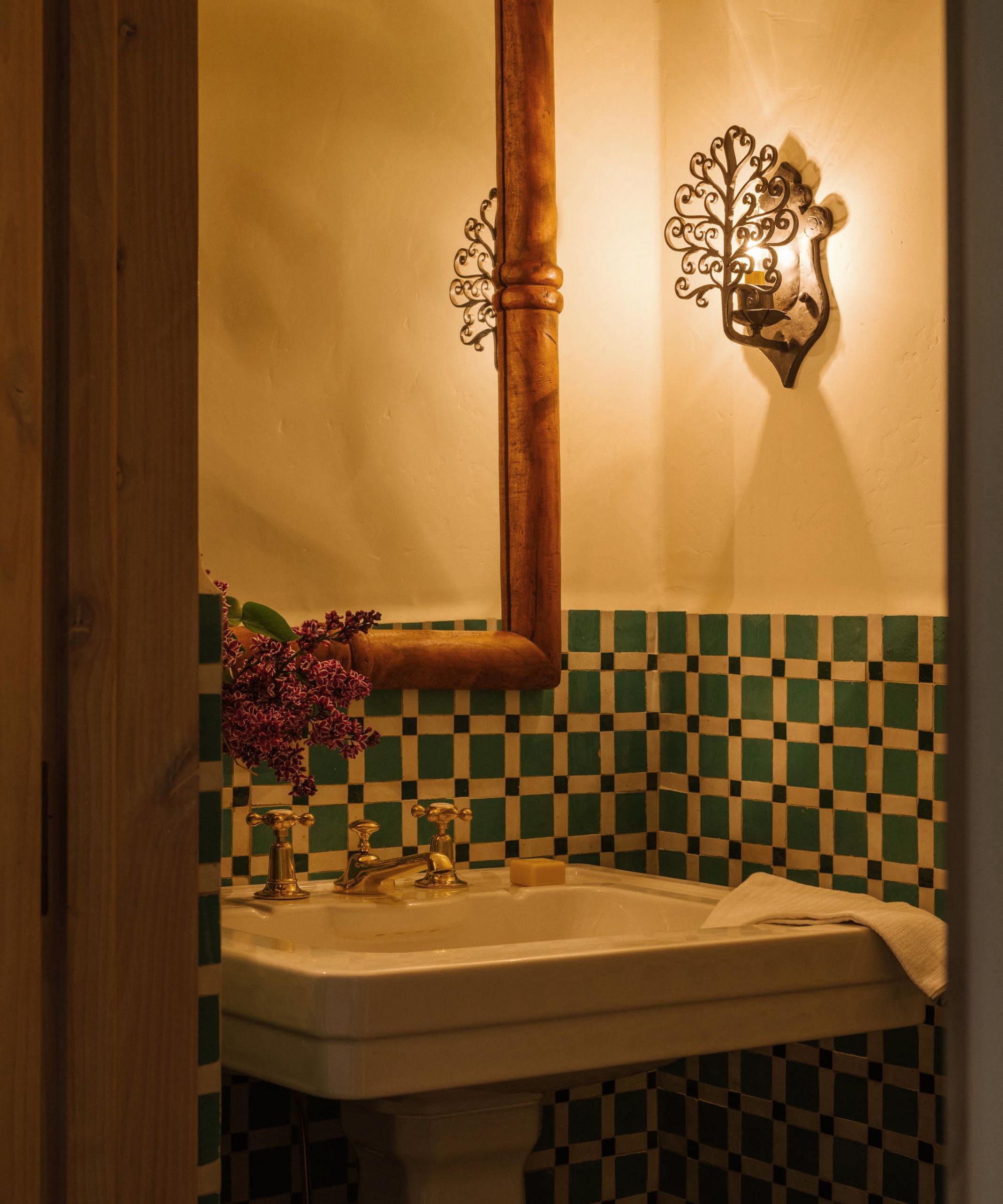 a small powder room with blue green mosaic half heigh tiles, a wooden mirror and small sink