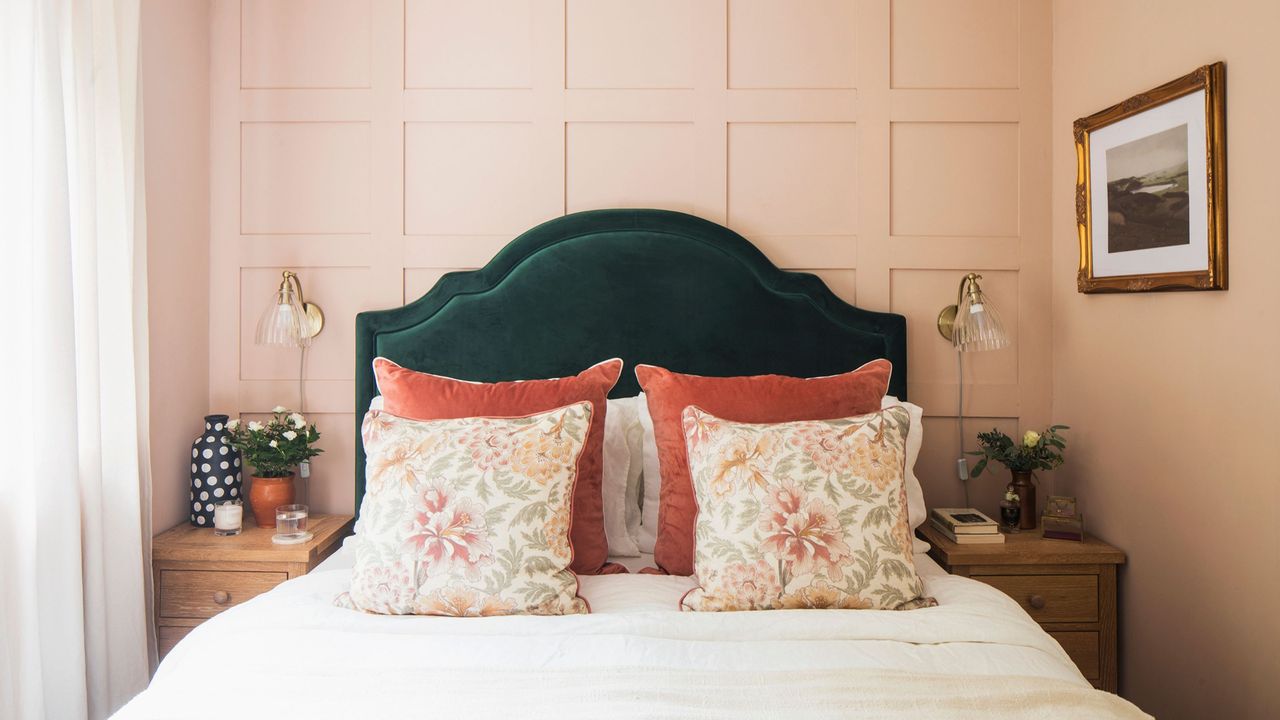 Pink painted bedroom with wall panelling behind the green bedframe, and cushions on the bed