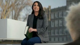 Cecily Strong sits on the logo while reading a book in Verizon.
