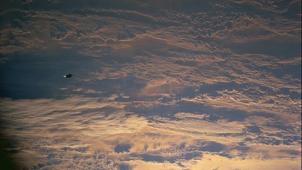 images captured from space show earth covered in clouds below and a small black object visible towards the left of the image.