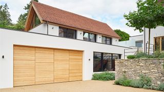 house with modern wooden garage doors incorporated into ground floor of house, rendered wall and gravel driveway in front