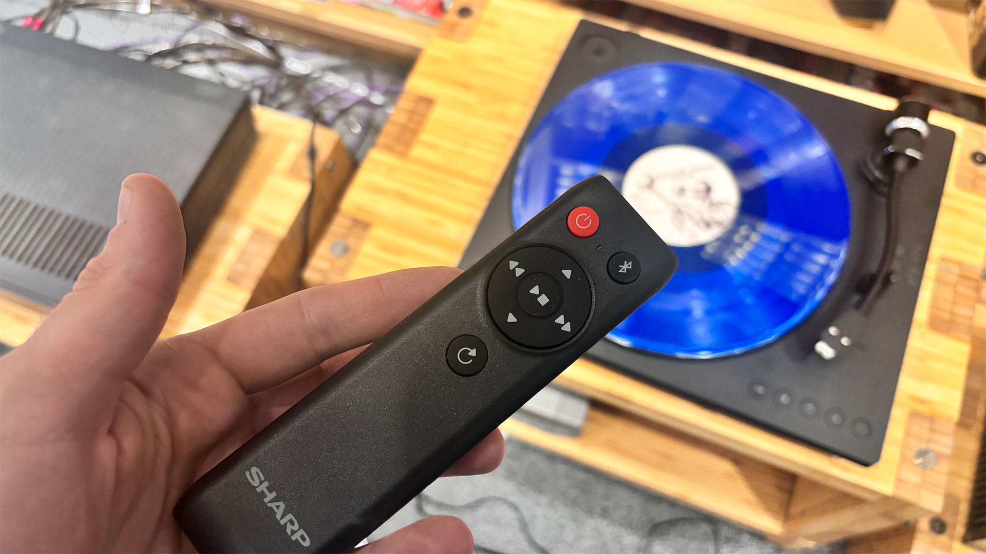 Sharp RP-TT100 Bluetooth turntable with blue vinyl on platter with remote control held in hand above