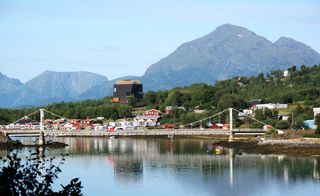 The Knut Hamsun Museum by Steven Holl, Norway. A dam with a wire bridge over it and buildings and hills behind it.