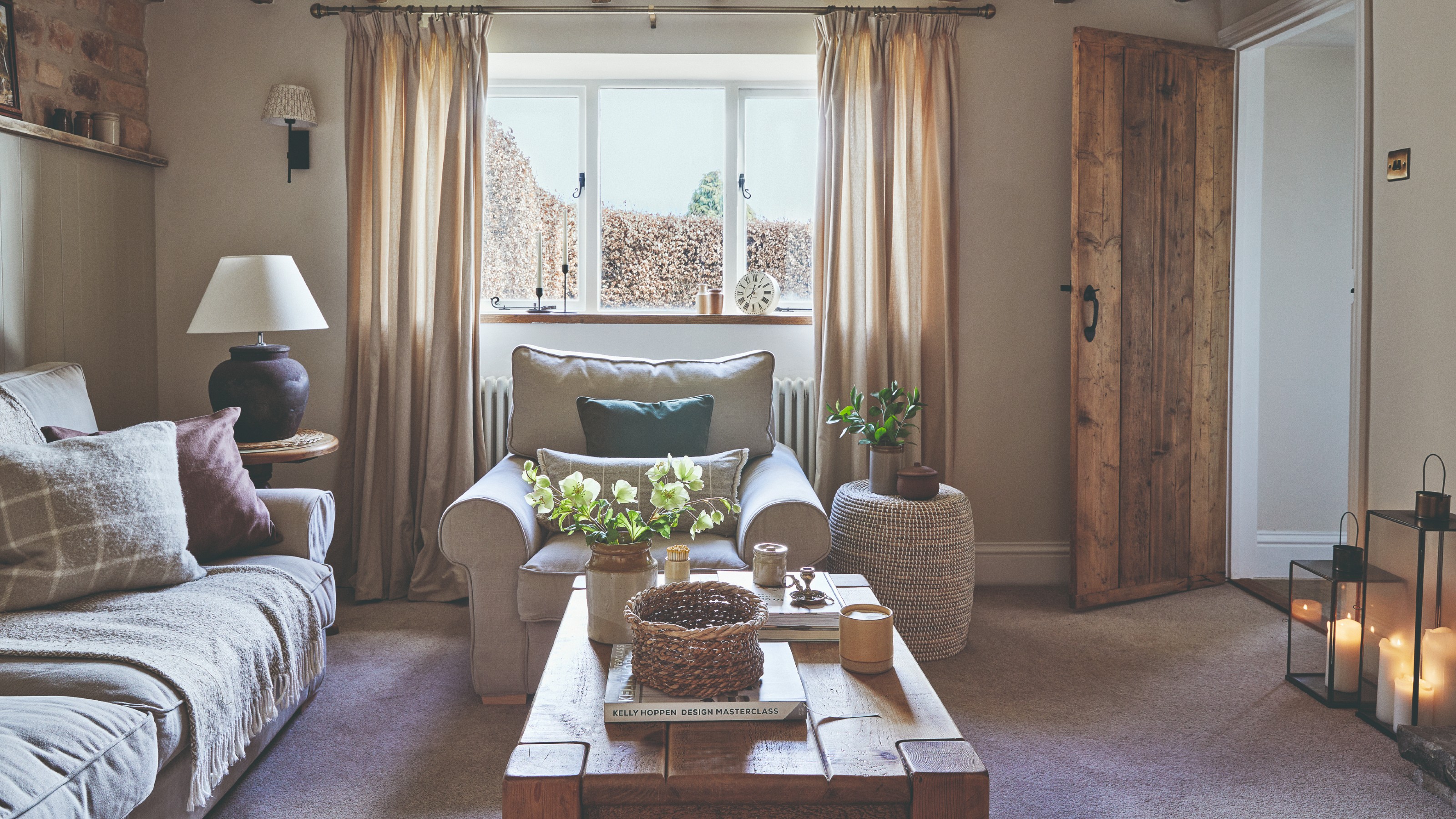 A cosy living room with a beige sofa layered with throws and cushions, a tonal armchair and a wooden coffee table