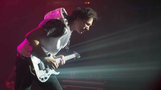 A photograph of Steve Vai on stage with a guitar