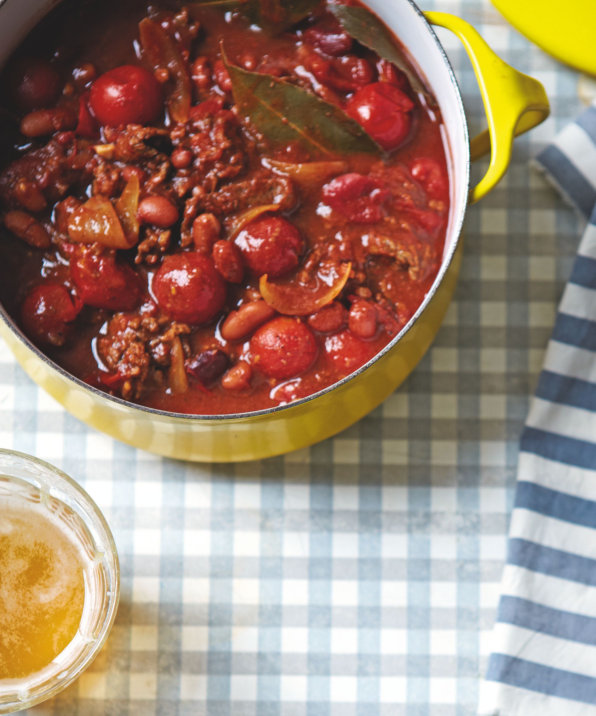 Chilli con carne in a yellow pan on a blue and white table cloth with a glass of beer