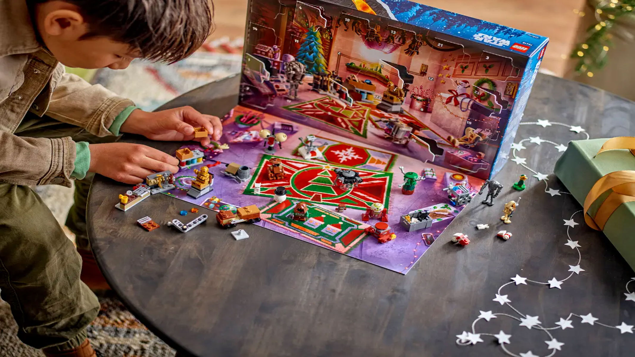 The contents of an advent calendar are splayed out in front of the calendar with a child playing with the brick-built toys on a table.