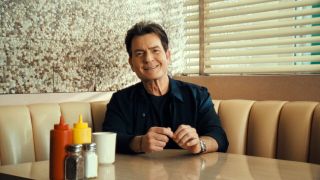 Charlie Sheen smiles while sitting in a booth in the trailer for the Netflix docuseries aka Charlie Sheen.
