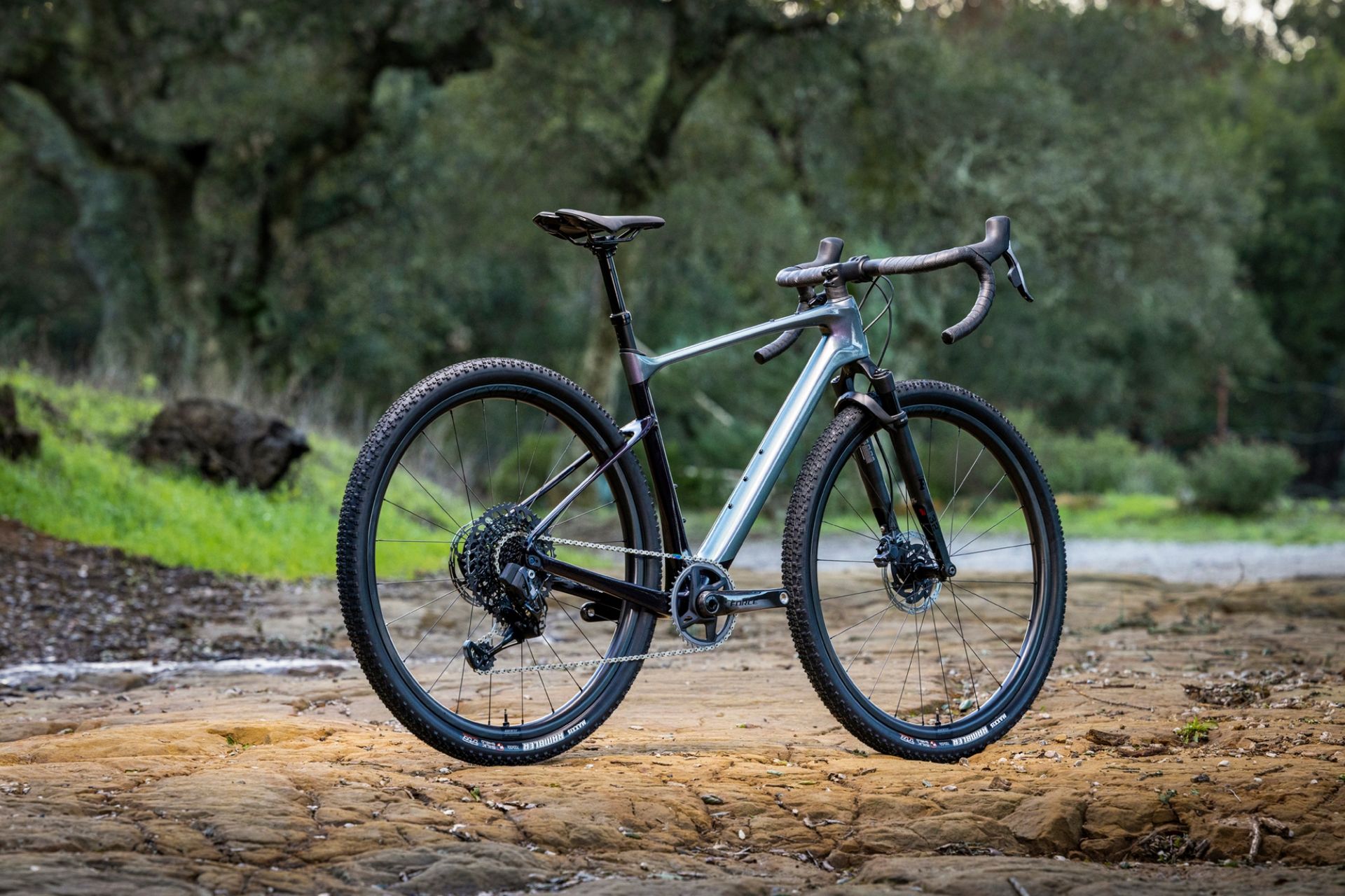 The all-new Giant Revolt X Advanced Pro 0 in full with brown soil under the wheels and green trees in the background