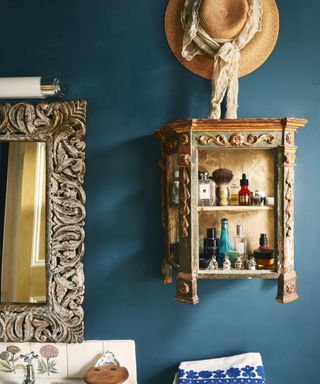 dark blue bathroom wall with ornate wooden shelf unit and matching mirror