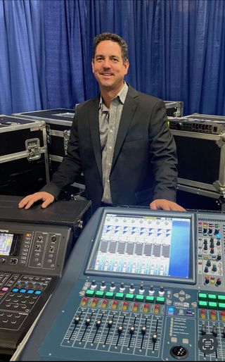 Andrew Shilo of AudioPros stands in front of a brightly lit mixer.