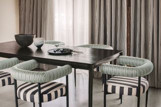 striped dining chairs around a table, finer striped curtains frame windows in the background