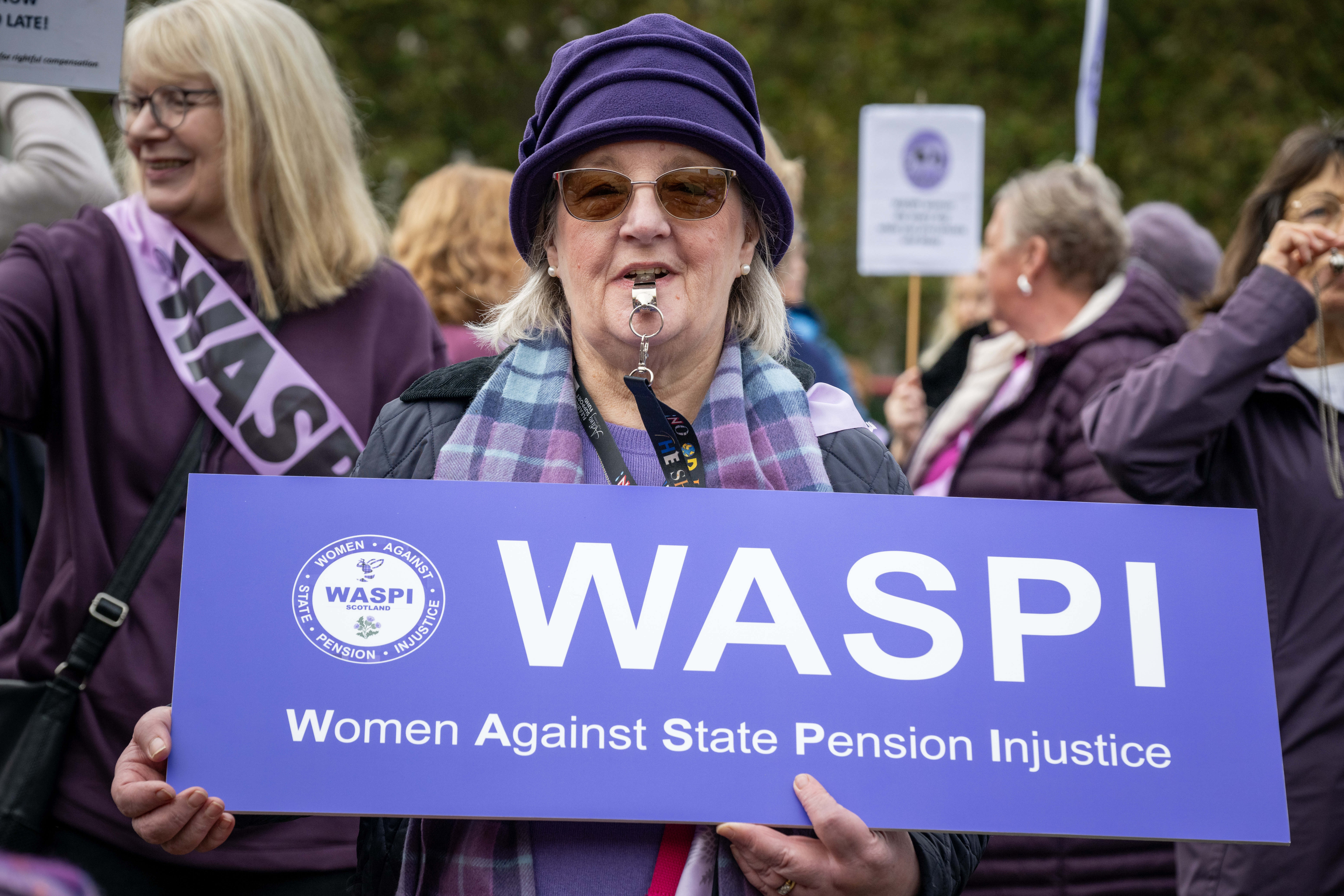 Retired women campaigning, one holding an official Women Against State Pension Injustice campaign sign with WASPI logo