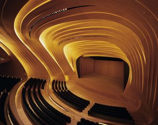 An auditorium featuring walls, ceiling and flooring with curved details created from strips of American oak. Black auditorium style seats