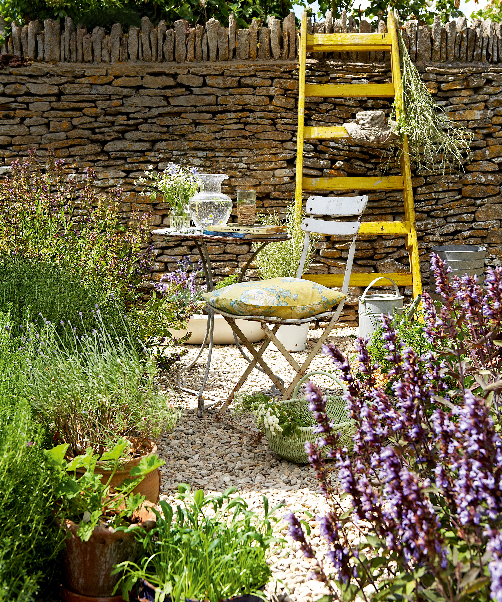Patio planting ideas with herbs in a small gravel courtyard with bistro table and chairs.