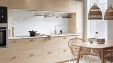 a light oak kitchen with several cabinets and drawers. There is a quartz/marble splashback and countertop. On the countertop is an induction hob with a pot on top. In the open plan kitchen there is also a dining table with boho style pendant lights above it. 