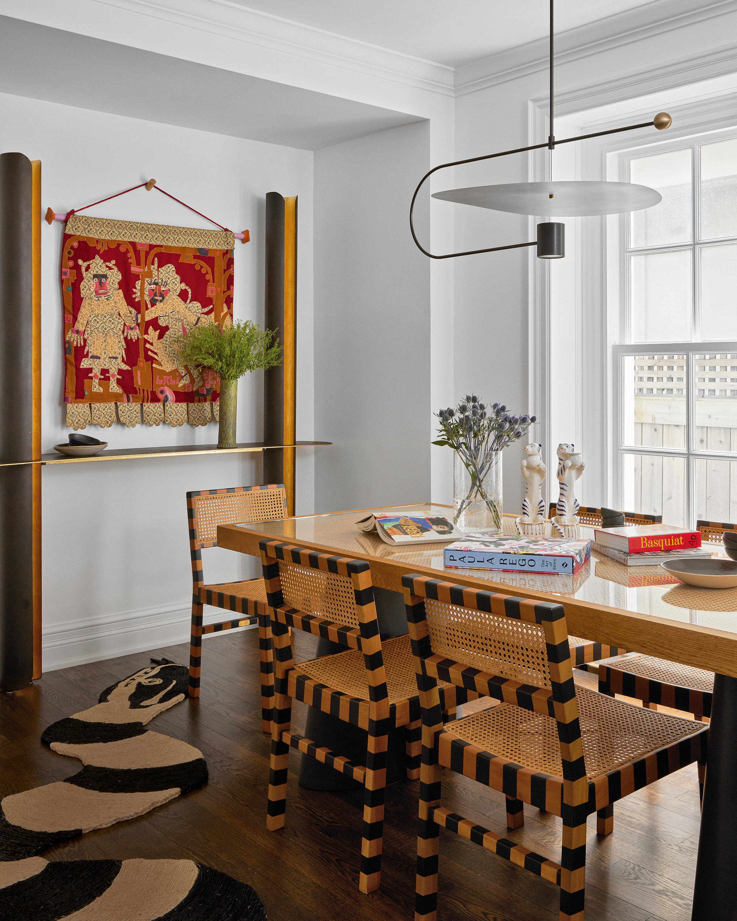 Dining room with wood table and black and orange checkerboard dining chairs, serpent sisal rug and tapestry artwork